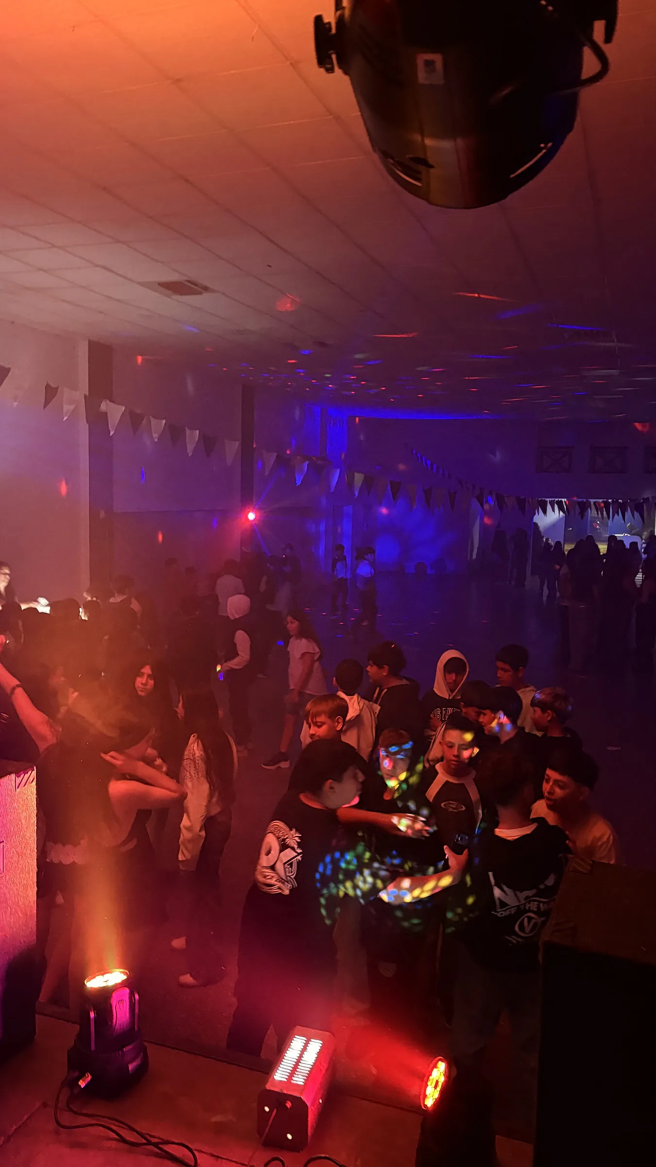 Público en la pista con luces cálidas y humo, cabezas móviles en primer plano